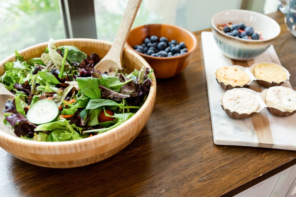 Fresh salad, blueberries, crackers, and small snacks arranged on a wooden table.